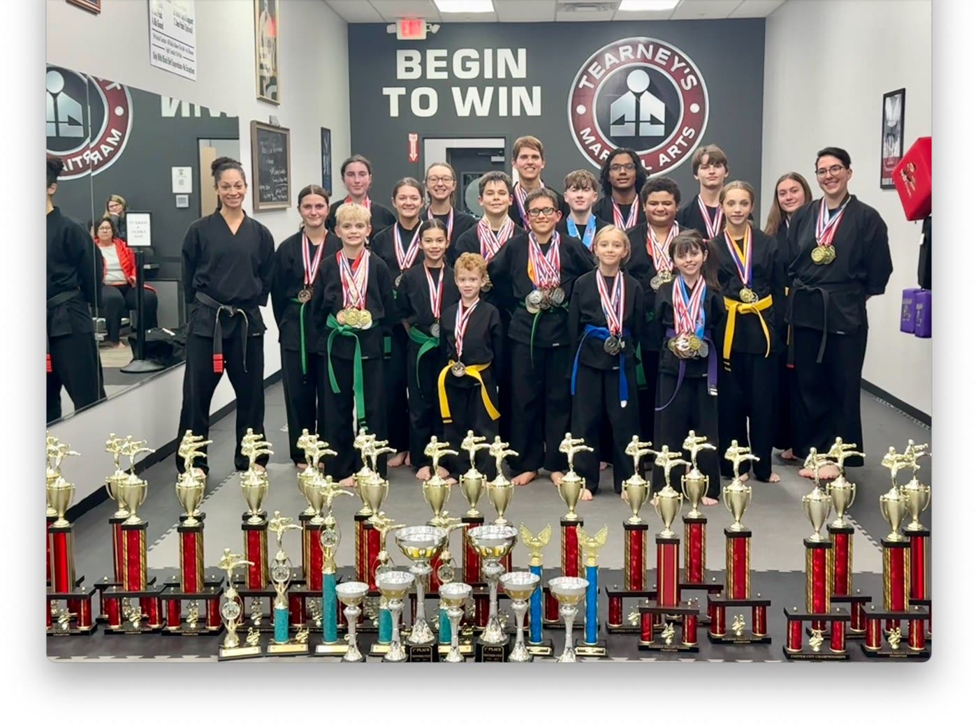 Team Tearney competitors with their medals and a display of championship trophies at the Camillus dojo